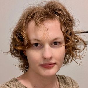 Headshot of Cassie, a person with shoulder-length, wavy light-brown hair, looking directly at the camera with a neutral expression.